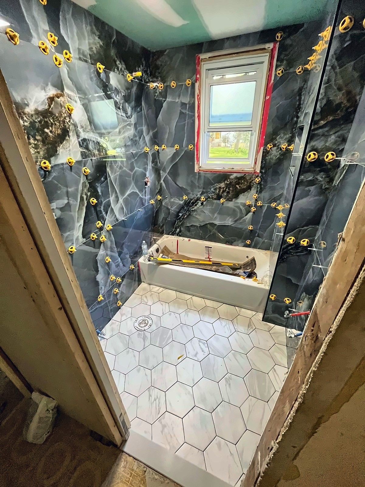 Bathroom mid-remodel with leveling clips on blue marble-look wall tile and a white hex tile floor