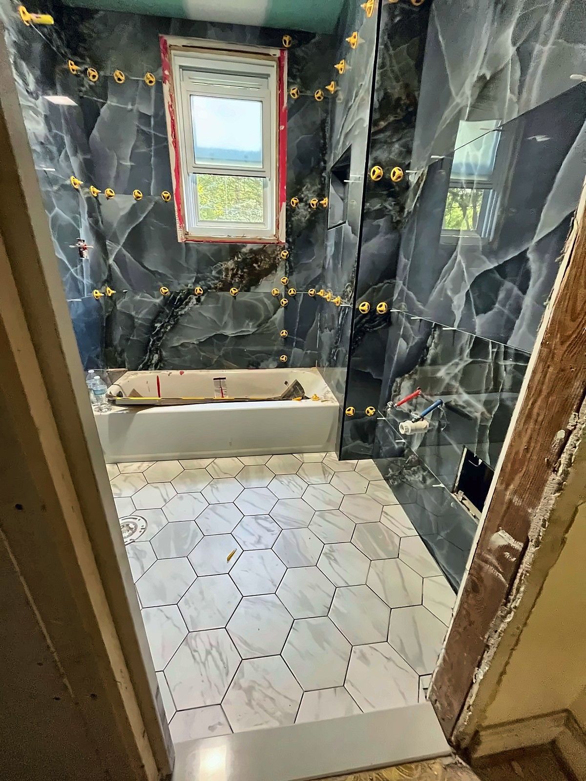 Bathroom tiling in progress with leveling clips, new tub and hex floor tile