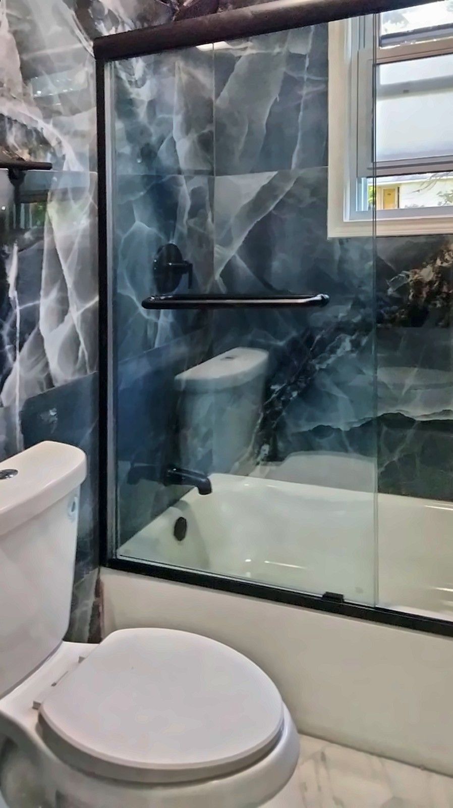Remodeled bathroom with toilet and glass-door tub in blue marble-look tile