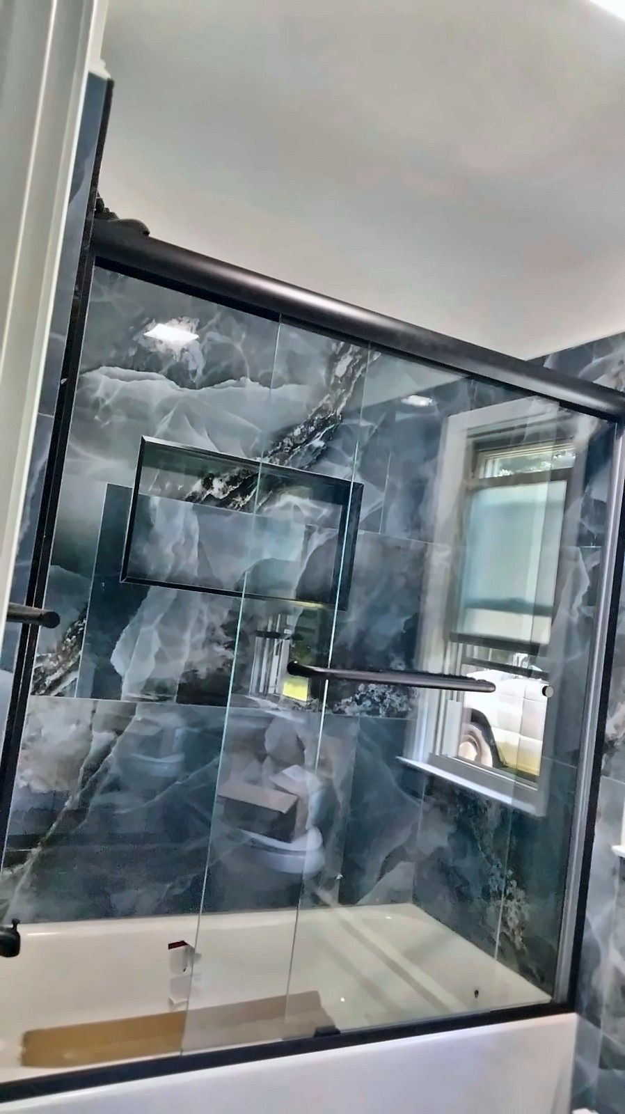 Angled view of a tub with glass doors and a tiled niche in blue marble-look tile