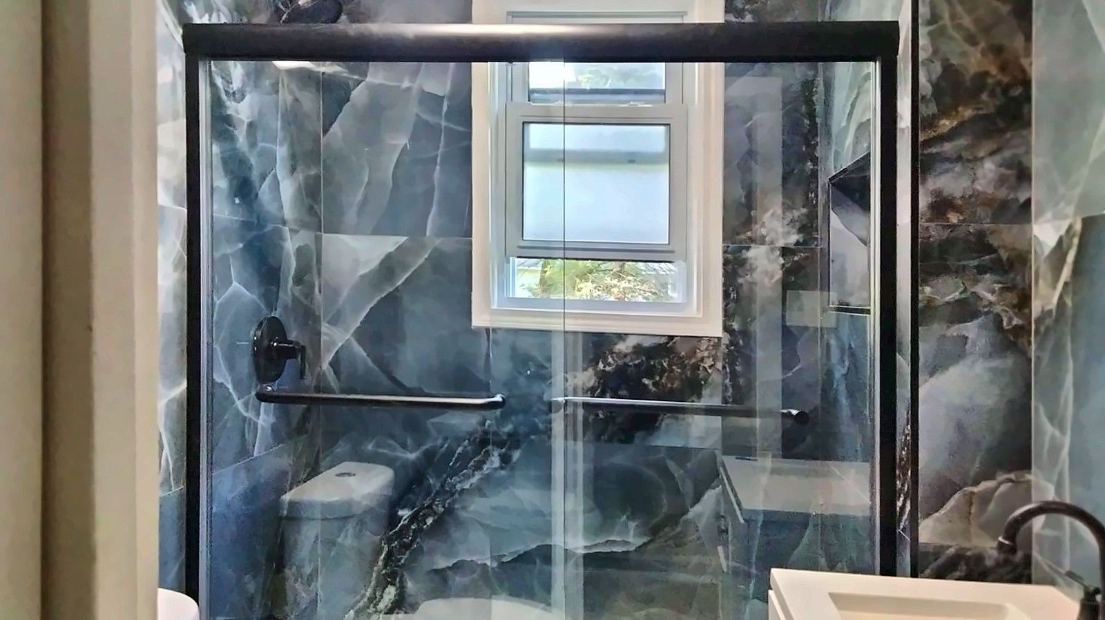 Bathroom with blue marble-look tile and a tub with black-framed glass doors