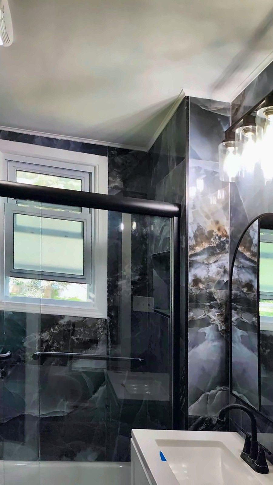 Bathroom with vanity, arched mirror and glass-door tub in blue marble-look tile