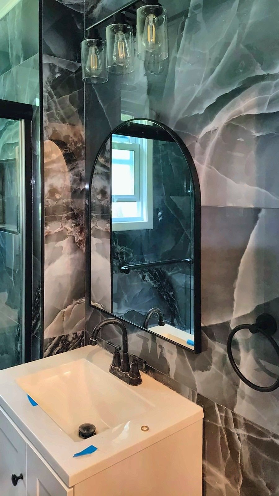 Vanity with arched mirror and glass-shade light in a blue marble-look tiled bathroom
