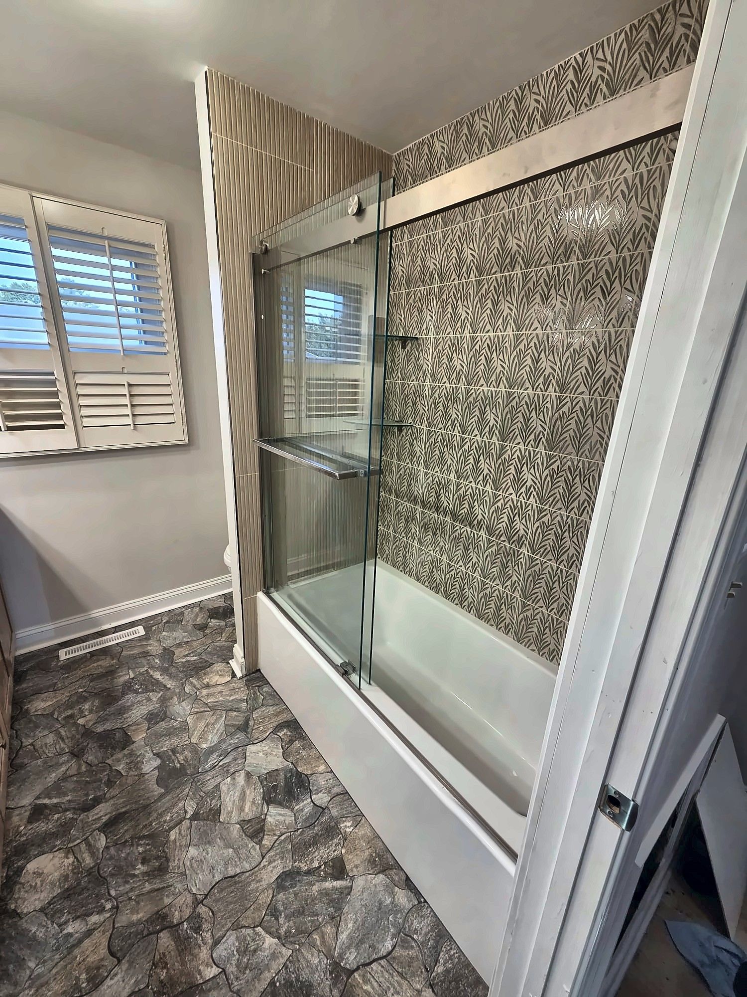 Tub with sliding glass doors and leaf-pattern tile wall