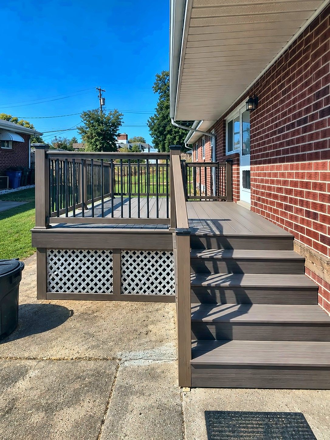 Composite deck and stairs with black metal railings at a brick home