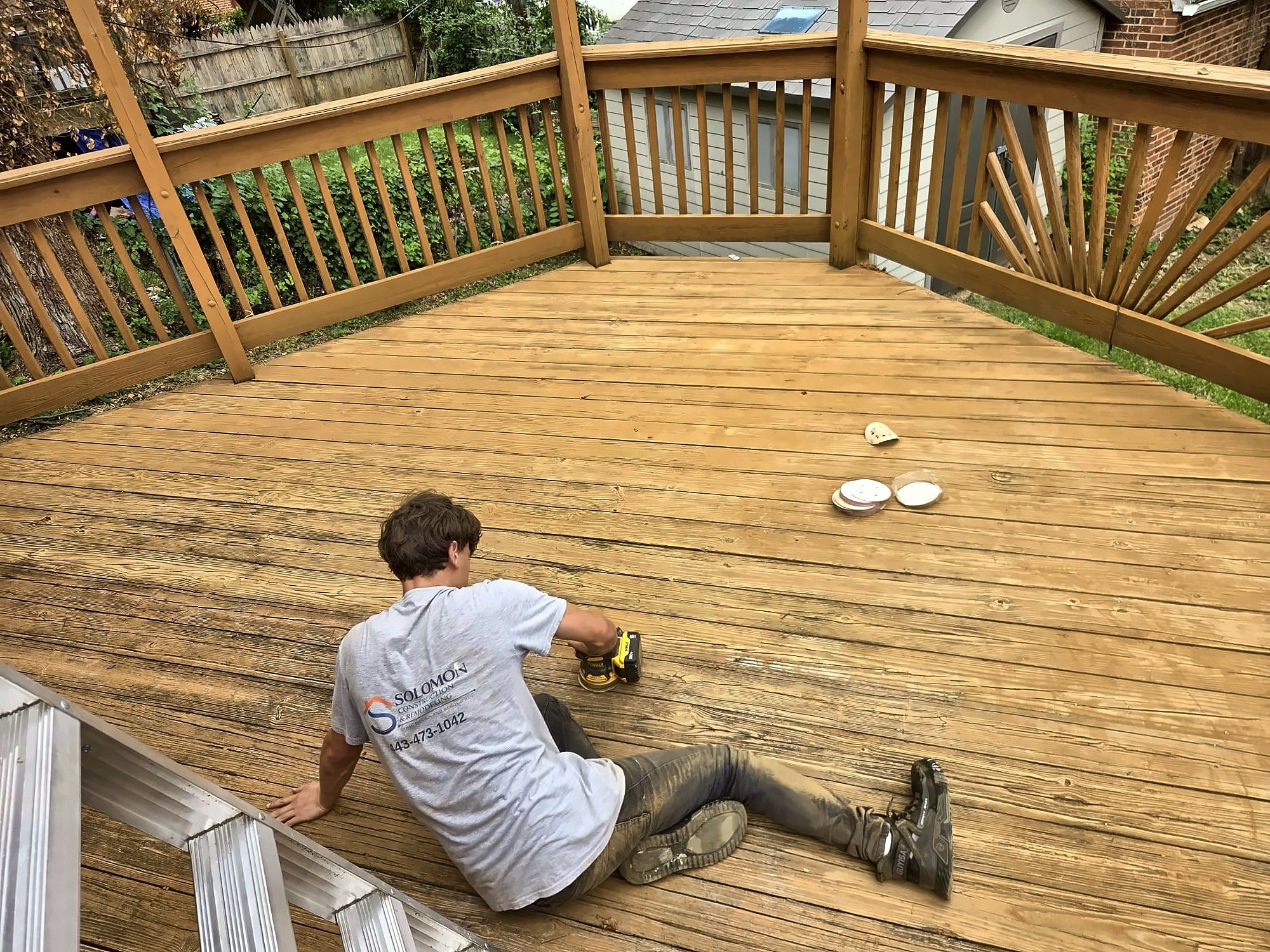 Crew member sanding a wood deck before refinishing