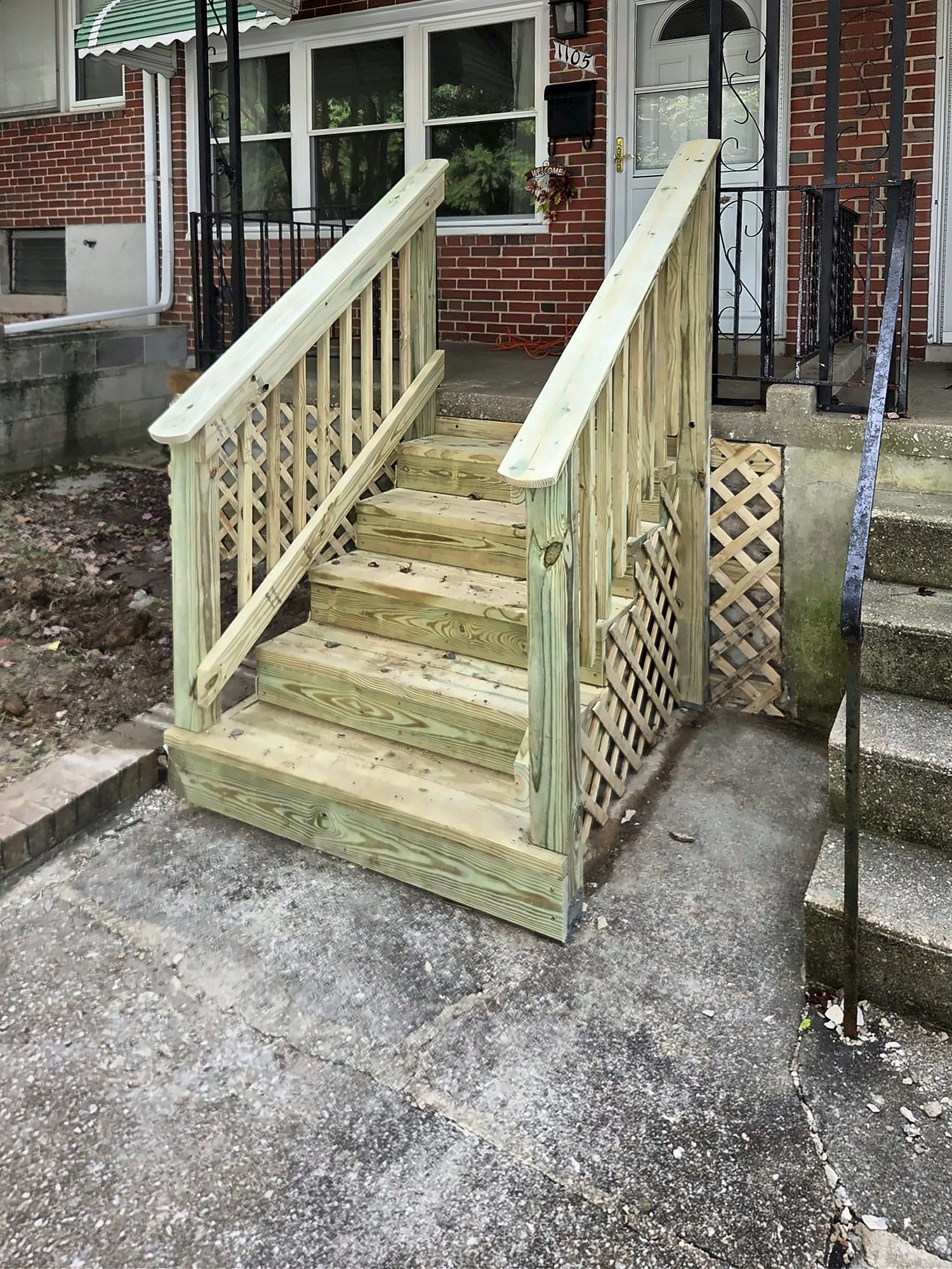 New pressure-treated wood front steps with railings at a brick rowhouse