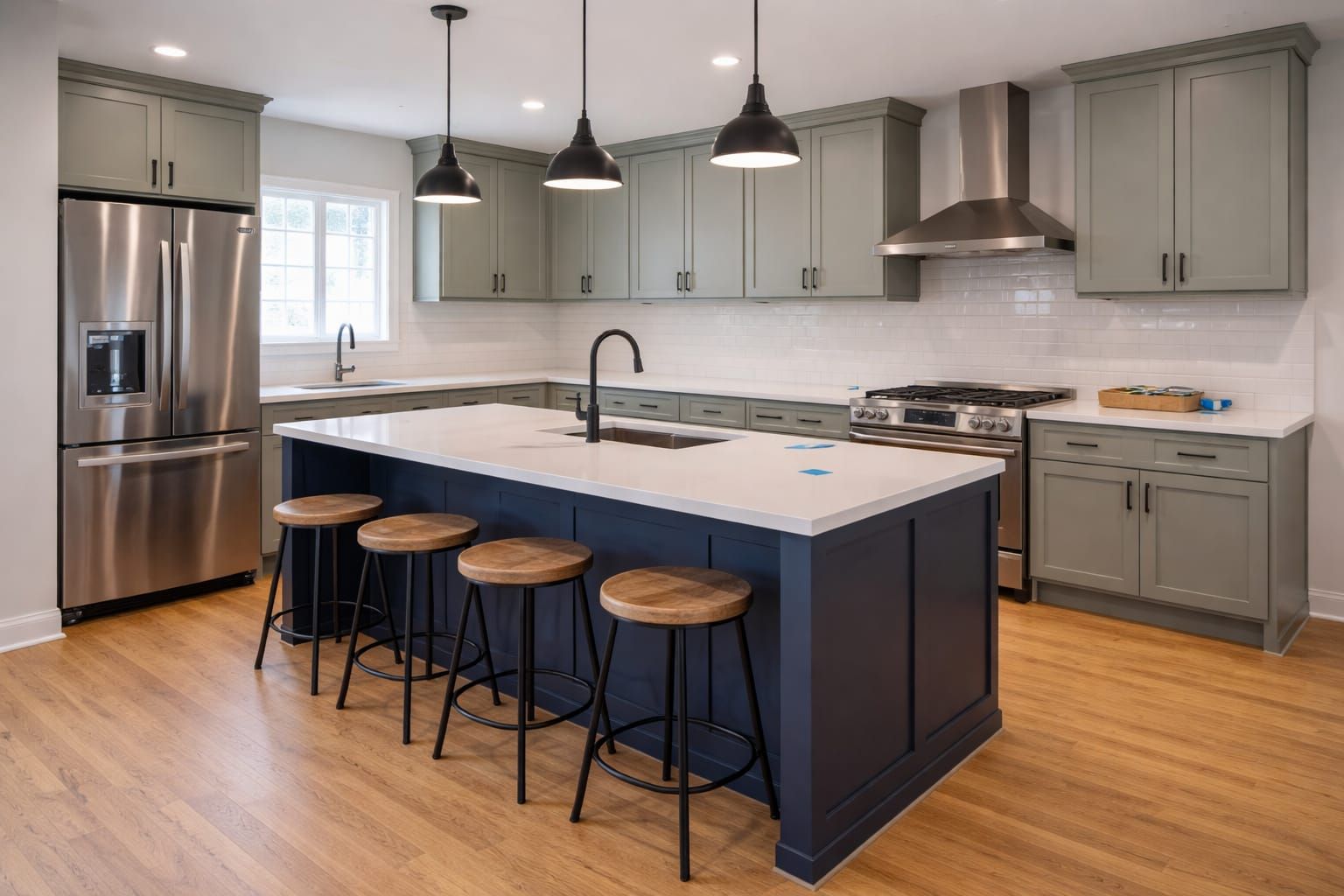 Kitchen with sage-green shaker cabinets, a navy island with four stools and black pendant lights