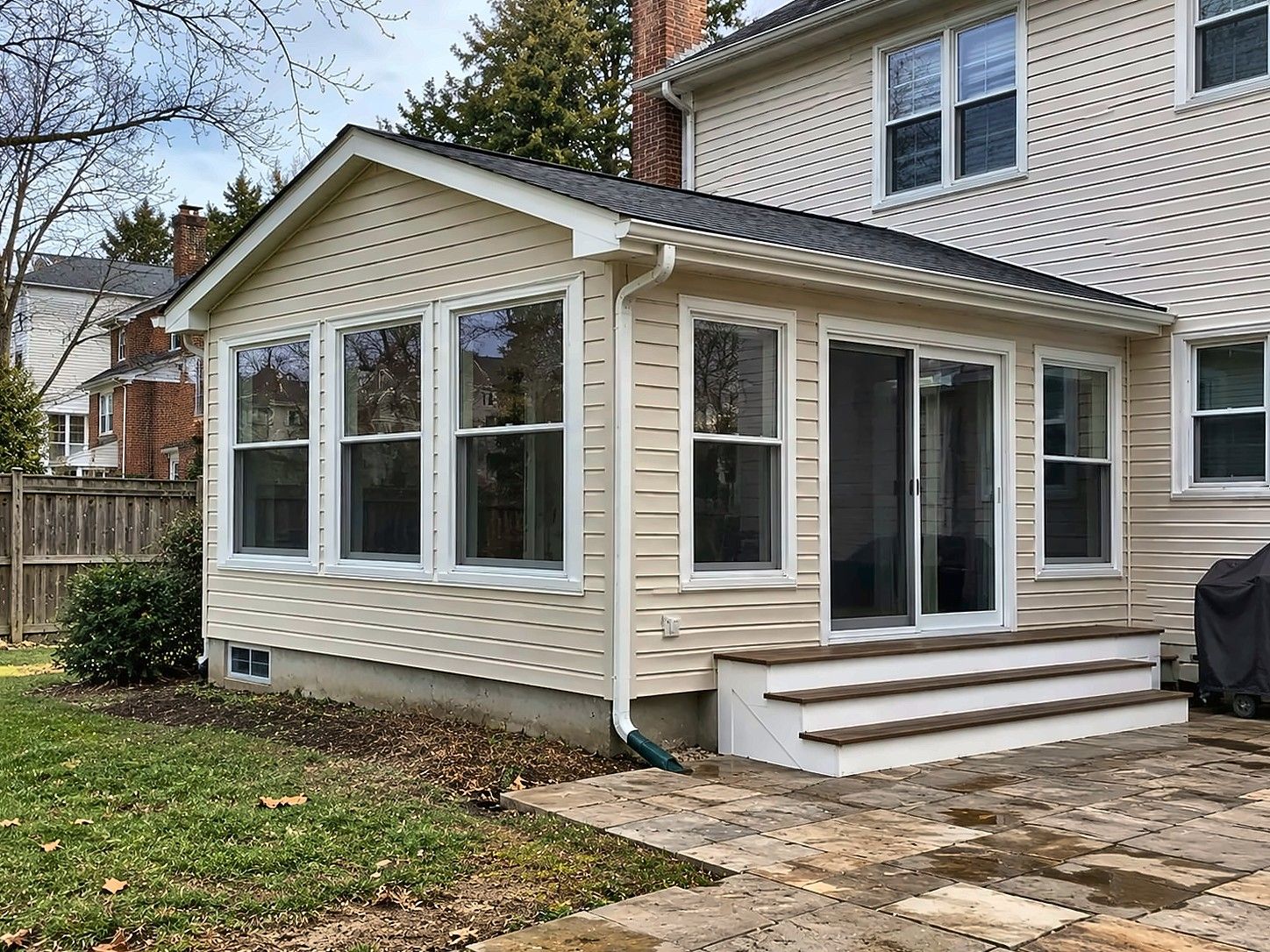 Rear room addition with cream vinyl siding, a row of windows and a sliding door with steps down to a stone patio