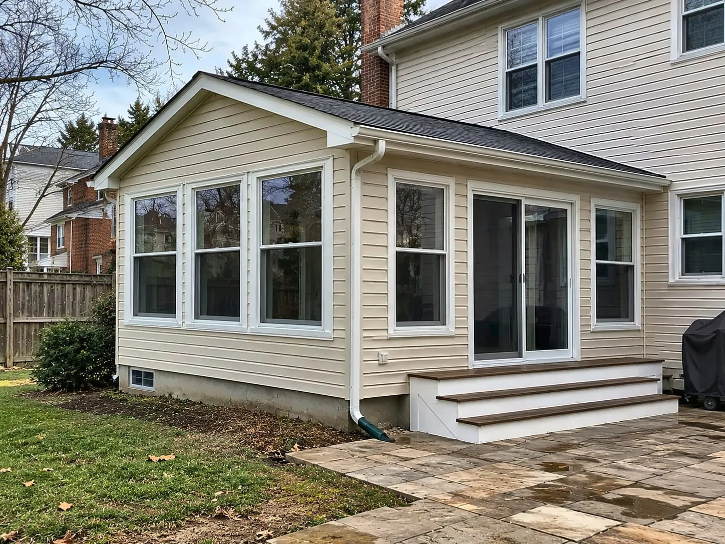 Rear room addition with cream vinyl siding, a row of windows and a sliding door with steps down to a stone patio
