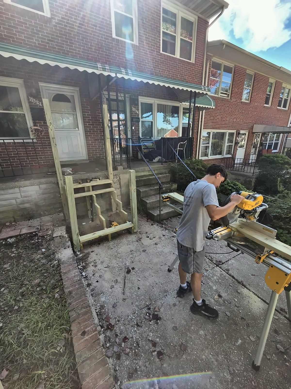 Crew member cutting lumber for new front steps at a brick rowhouse